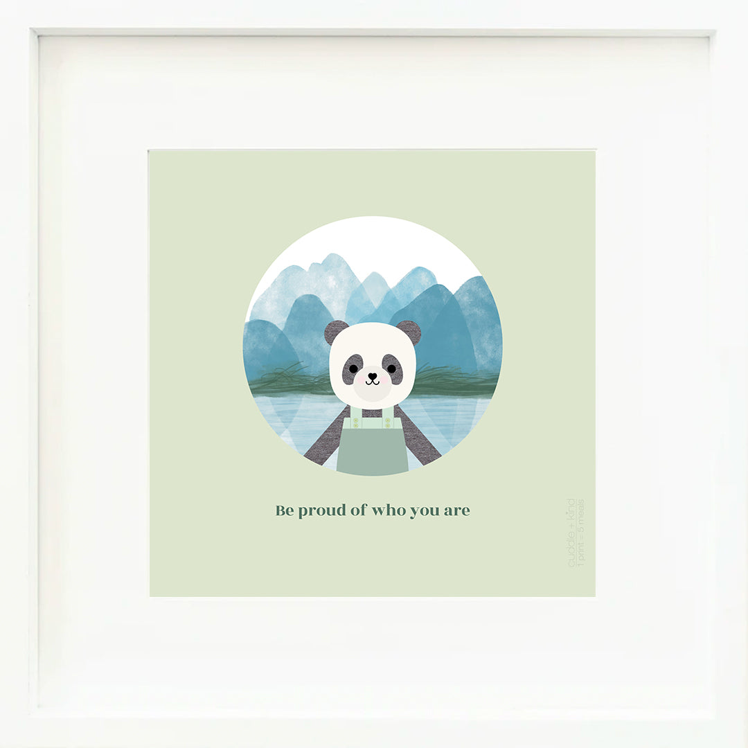 An inspirational print with a graphic of Paxton the panda in front of a mountainous landscape of blue watercolour. The background of the print is jade with the words “Be proud of who you are” in darker green.
