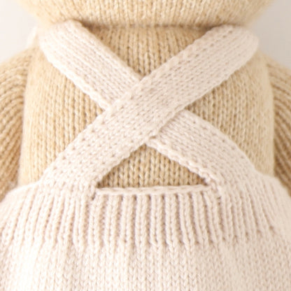 A close-up showing the criss-crossed straps on the back of Goldie the honey bear’s mushroom-shade apron dress.