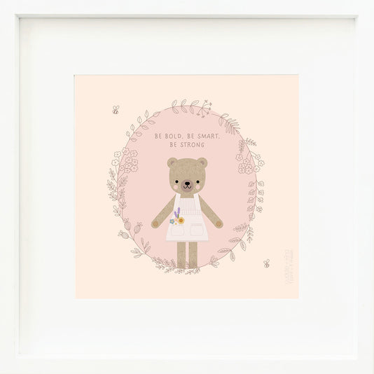 An inspirational print with a graphic of Goldie the honey bear in a circle of floral and leafy vines with a pair of bumblebees. The background is purple and pink and above Goldie’s head are the words “Be bold, be smart, be strong”