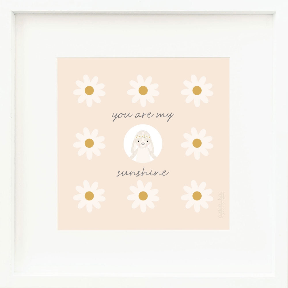 An inspirational print with a graphic of Hannah the bunny in ivory, on a light orange background decorated with daisies and the words “You are my sunshine” in dark gray.