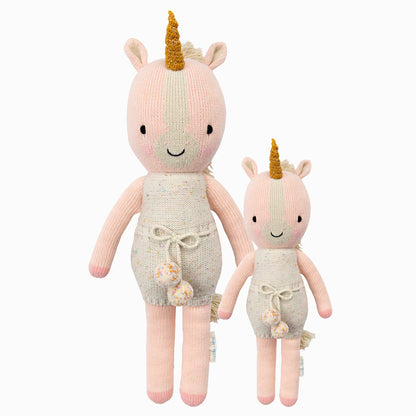 Ella the unicorn in the regular and little sizes, shown from the front. Ella is wearing a white romper with confetti polka dots and a pom-pom waist tie.