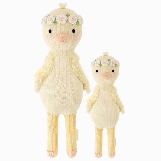 Flora the duckling in the regular and little sizes, shown from the front. Flora has yellow feathers and is wearing a pair of pink ballet slippers and an ivory flower crown with soft yellow centers and green leaf details.