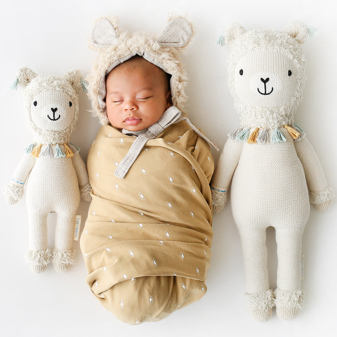 A sleeping baby snuggled between two Lucas the llama stuffed dolls in the little and regular sizes.