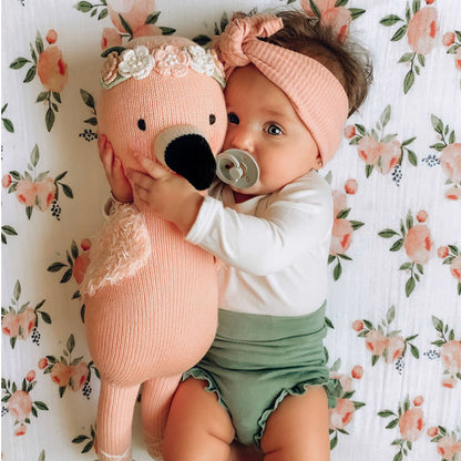 A baby in a soft, pink headband snuggling with Penelope the flamingo.
