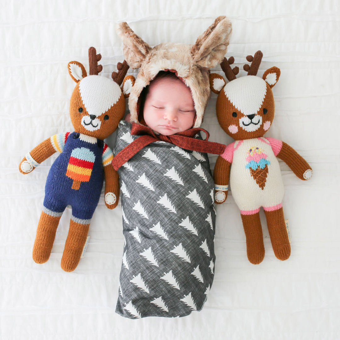 A sleeping baby in a fluffy deer hood, nestled between Scout and Willow the deer stuffed dolls. 