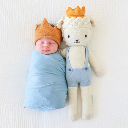 A sleeping baby with Sebastian the lamb in the regular size. The baby has a knitted crown to match Sebastian.