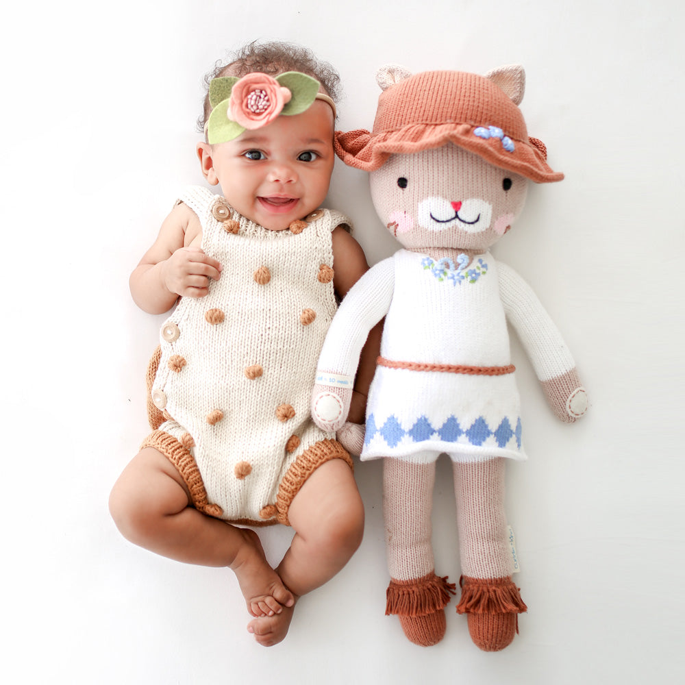 A smiling baby in a knit onesie with a Chelsea the cat doll.