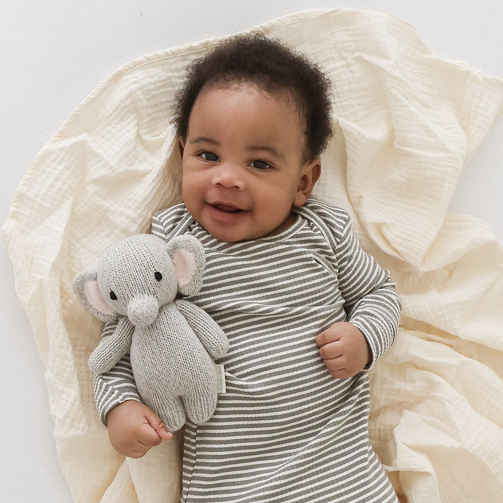 A smiling baby holding a baby elephant stuffed animal.
