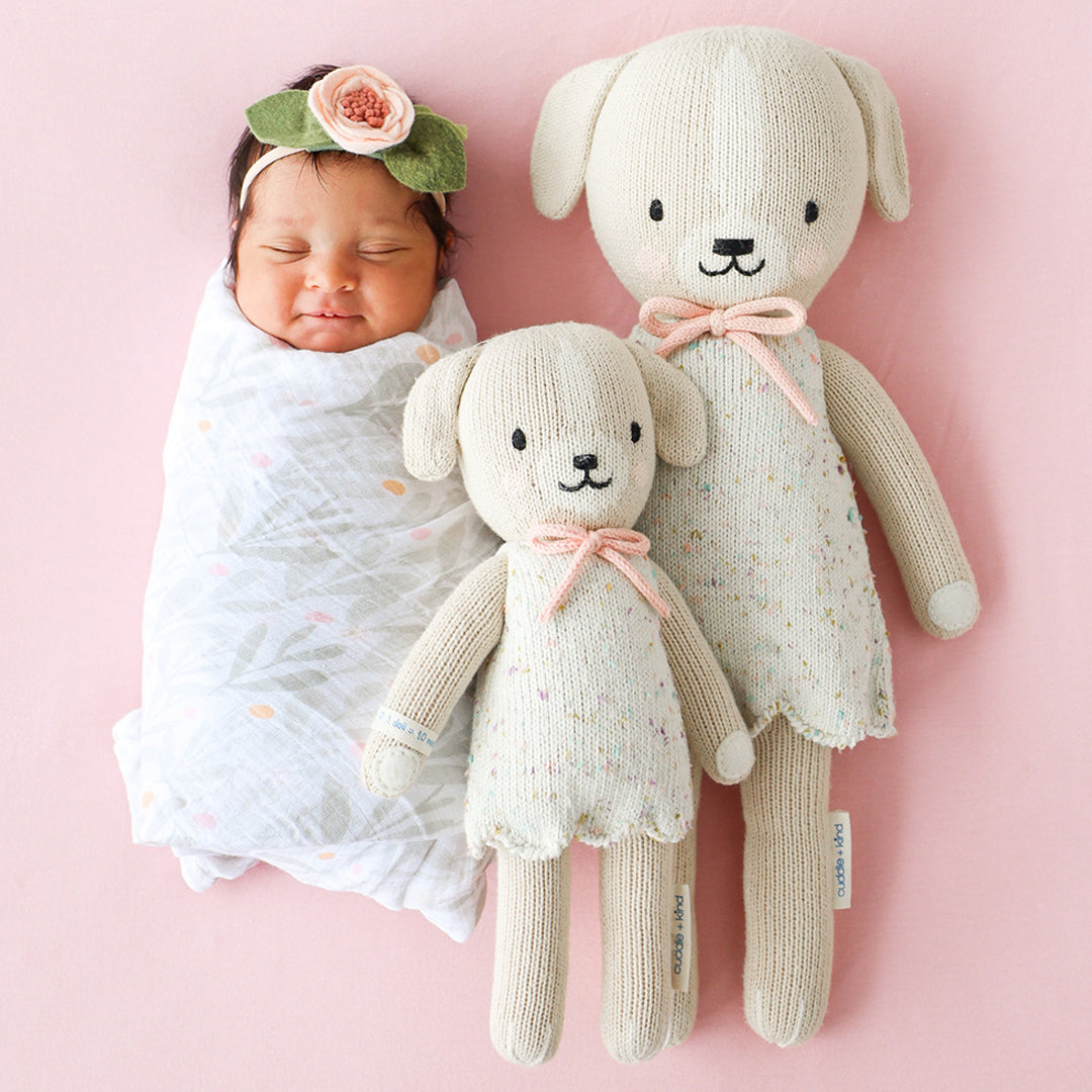 A sleeping baby lying side-by-side with two Mia the dog dolls in the little and regular sizes.