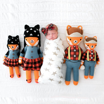 A sleeping baby wearing a plaid bow, lying between four hand-knit stuffed animals: Sadie and Wyatt the foxes, in the little and regular sizes.
