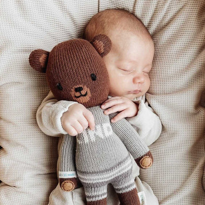 A sleeping baby cuddling with Oliver the bear.
