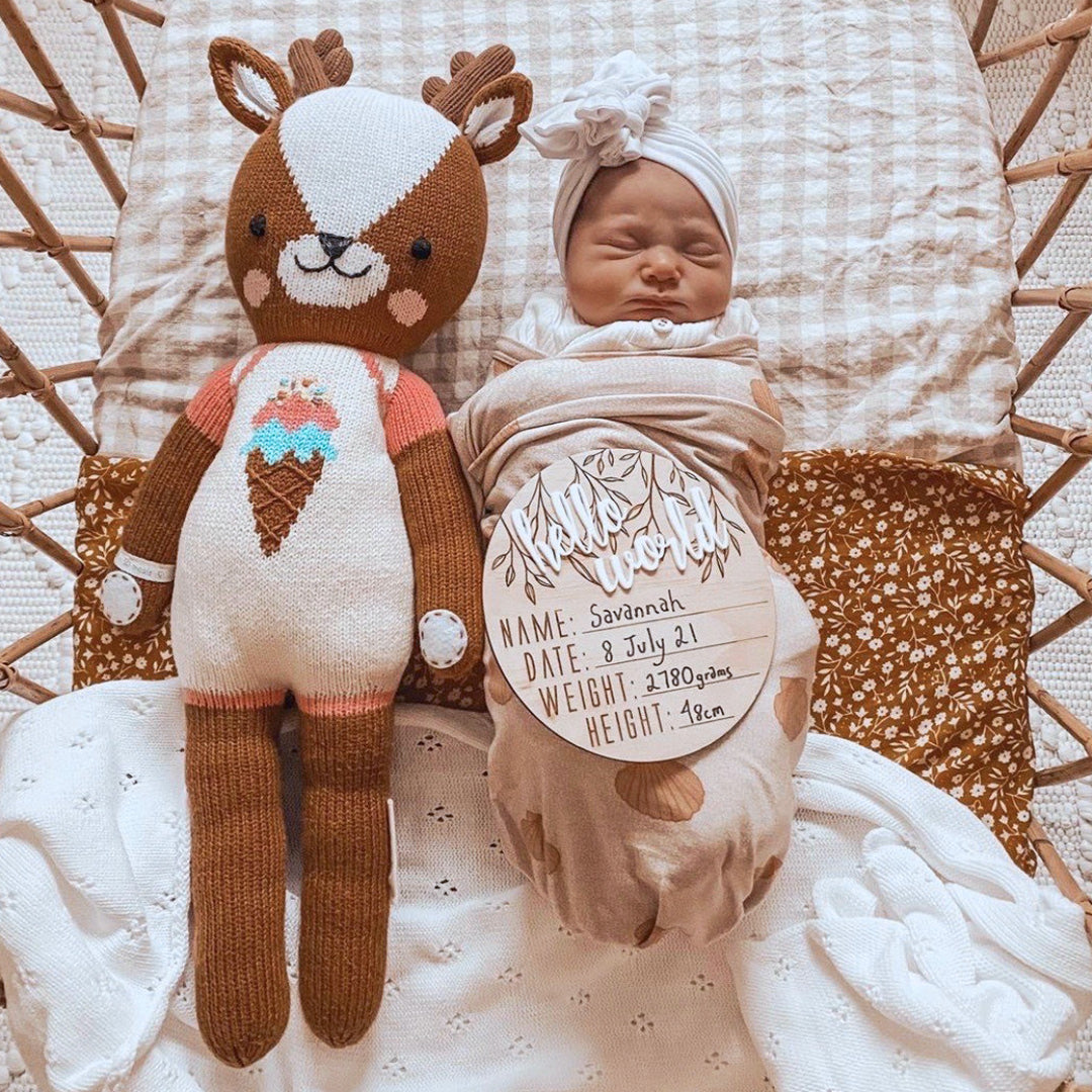 A swaddled, sleeping baby snuggled beside a Willow the deer stuffed doll.
