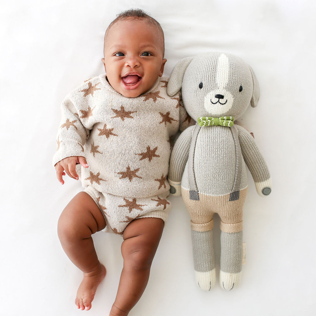 A laughing baby holding a Noah the dog stuffed doll.