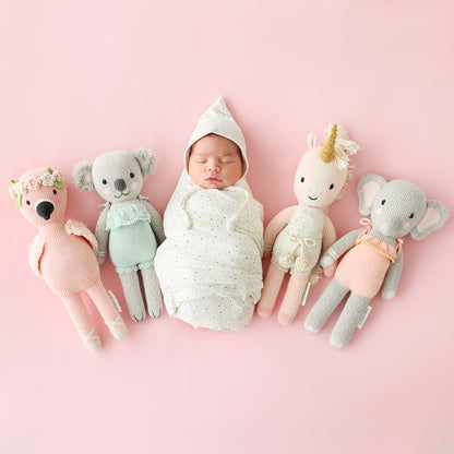 A sleeping baby lying between four cuddle and kind hand-knit dolls.