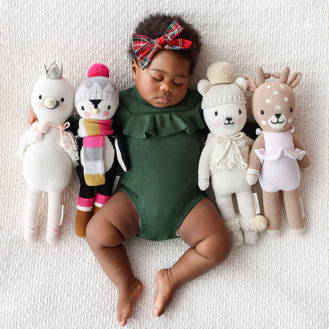 A sleeping baby with their arms around four cuddle and kind hand-knit dolls.