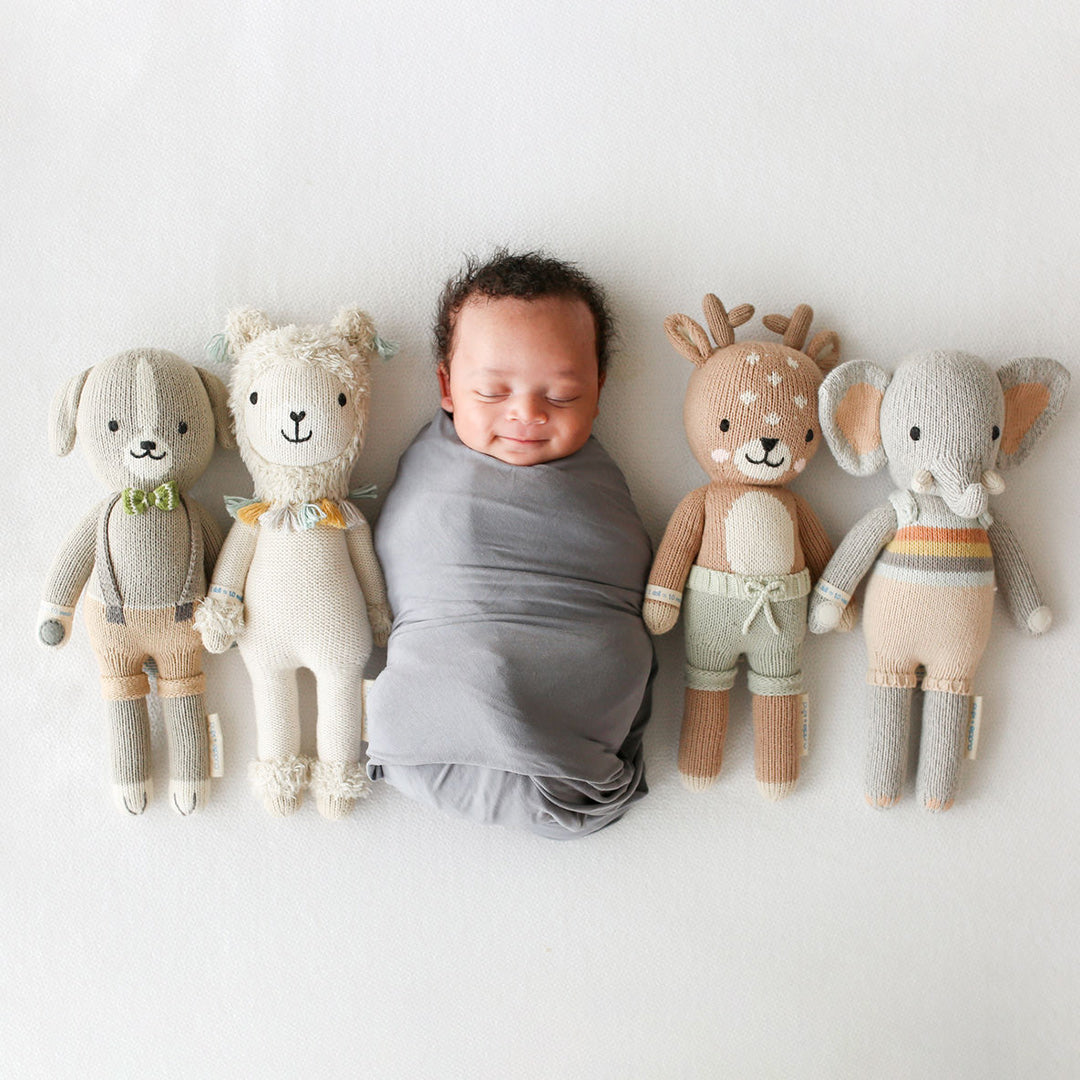 A sleeping baby lying in a row with four hand-knitted dolls: Noah the dog, Lucas the llama, Elliott the fawn and Evan the elephant.