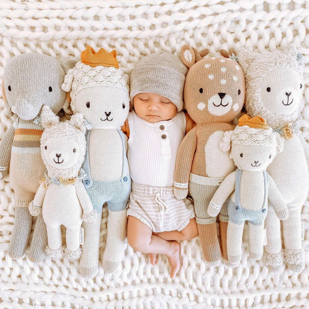 A sleeping baby snuggled in the middle of six cuddle+kind stuffed dolls.