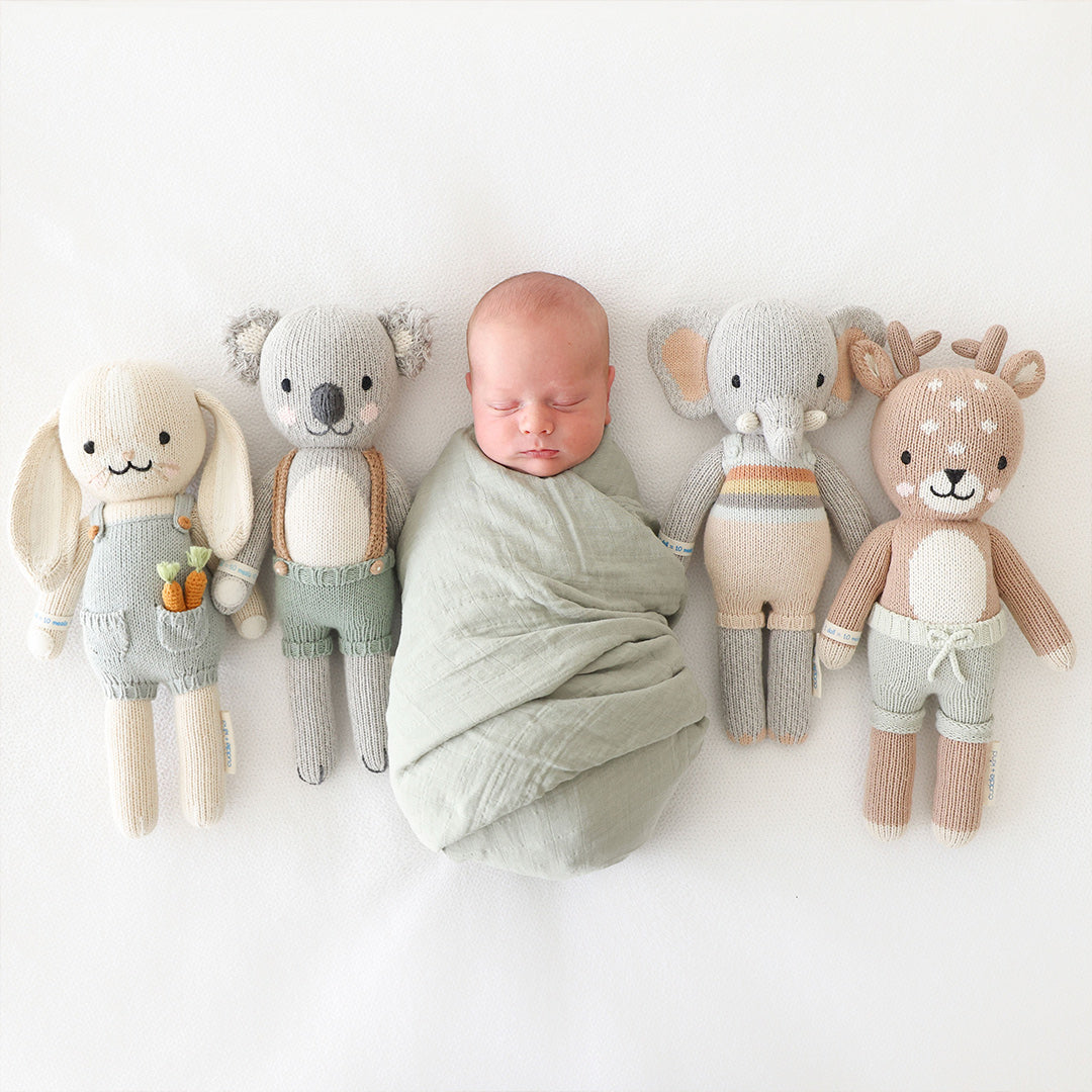 A sleeping baby in the middle of four cuddle+kind stuffed dolls: Henry, Quinn, Evan and Elliot. 