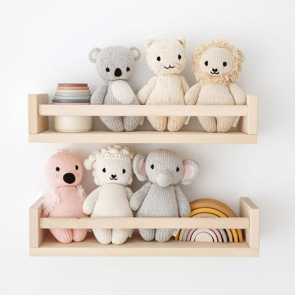 Six of the dolls in the baby animal collection sitting on two wooden shelves next to baby toys.