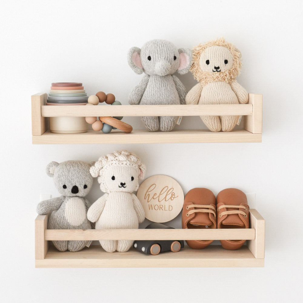 Four dolls from the baby animal collection sitting on wooden shelves next to baby toys, shoes and a sign that says “hello world.”