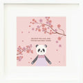 An inspirational print with a graphic of Polly the panda between the limbs of a flowering cherry tree on a pink background with the words “Believe you can, and you’re halfway there” in currant.