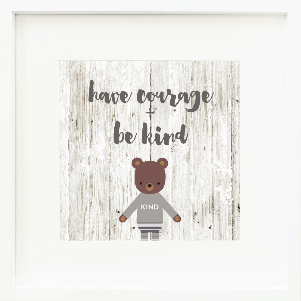 An inspirational print with a graphic of Oliver the bear on a textured wood background with the words “Have courage + be kind” in dark gray.