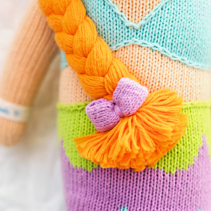 A close-up showing the hand-knit details on Isla, including the purple bow on her yarn braid.