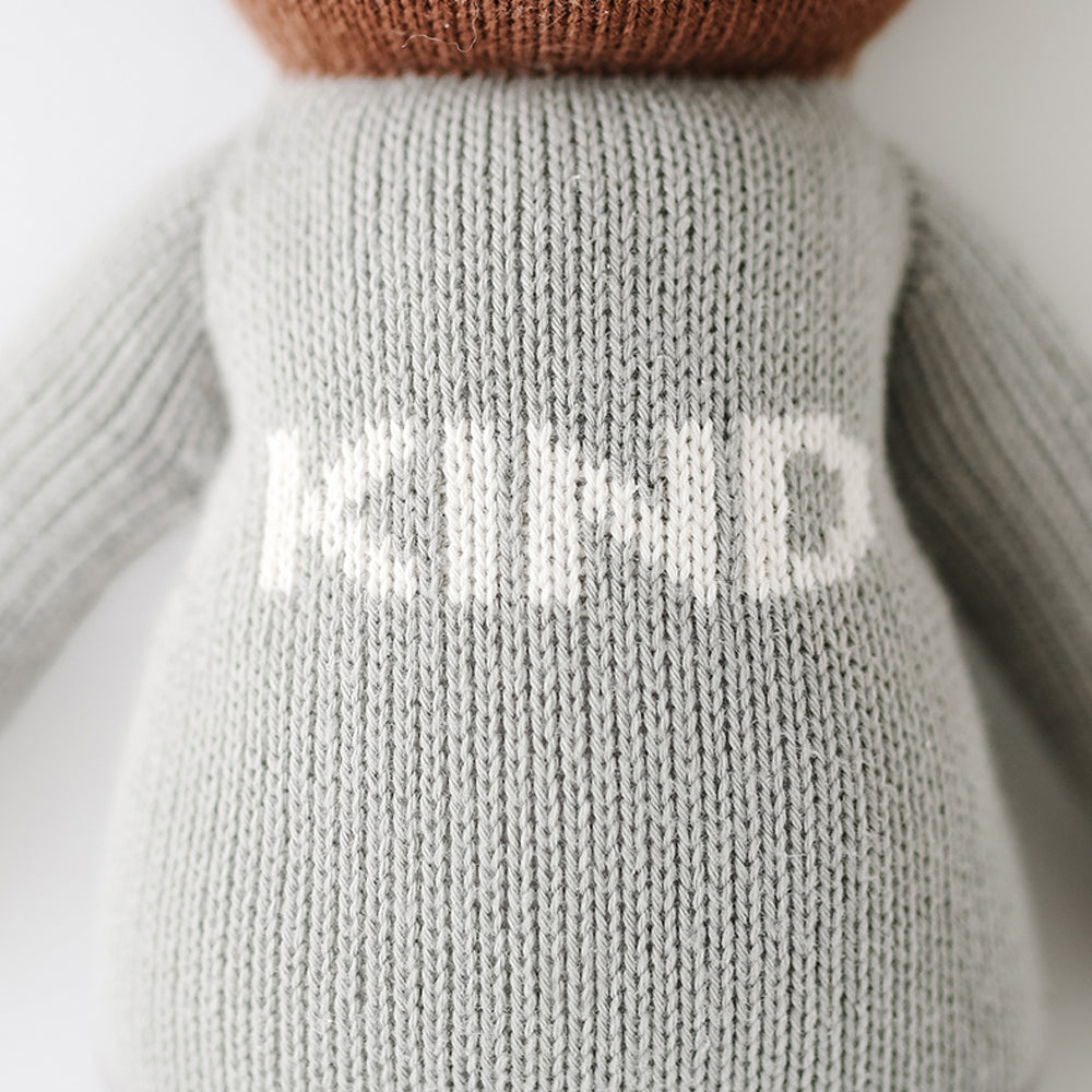 A close-up showing the hand-knit details on Oliver’s sweater that has the word “Kind” on it in white letters.