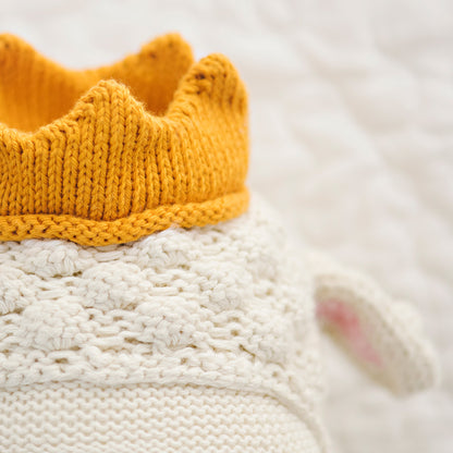 A close-up showing hand-knit details on Sebastian the lamb’s head, and his golden-yellow knitted crown.