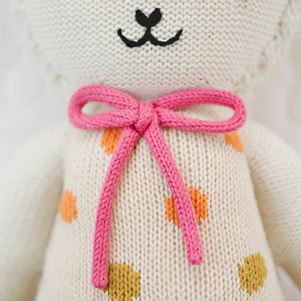 A close-up showing hand-knit details on Lucy the lamb, including her pink yarn bow.