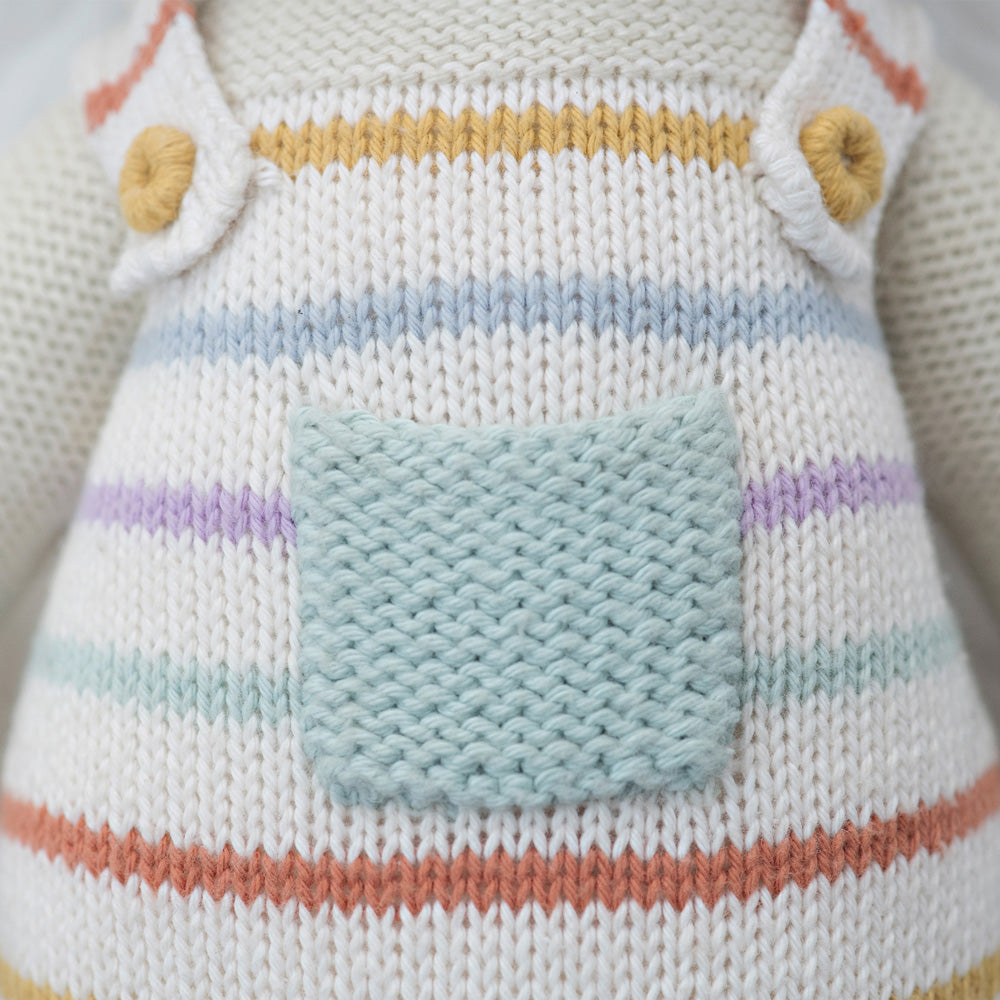 A close-up showing hand-knit details on the overalls Avery the lamb doll is wearing.