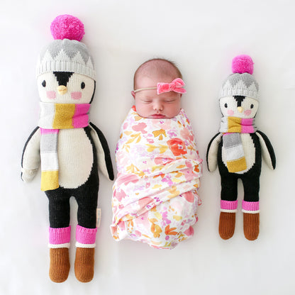 A sleeping baby lying in between two Aspen the penguin dolls in the regular and little sizes.