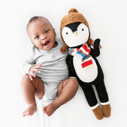 A smiling baby with his arm around an Everest the penguin stuffed doll. 