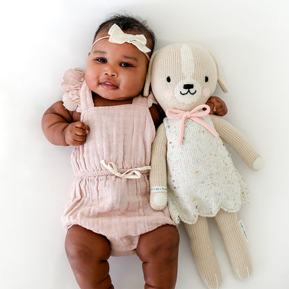 A baby with her arm around Mia the dog. The baby is wearing a bow headband to match Mia's bowtie.  