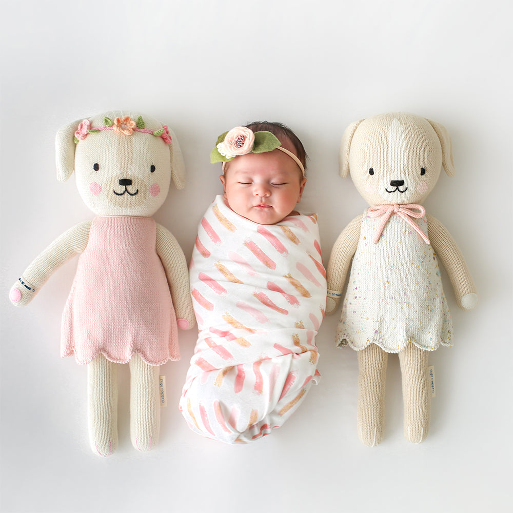 A sleeping baby in between two knit stuffed dolls, Charlotte the dog and Mia the dog.