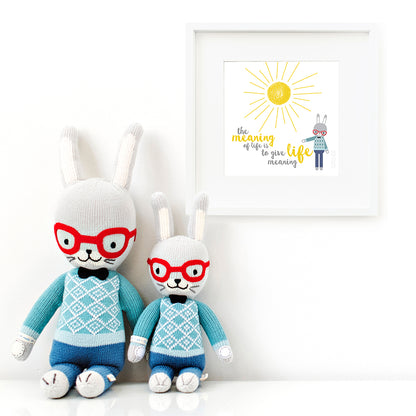 Two Benedict the bunny stuffed dolls sitting beside a framed print with a picture of Benedict that says “The meaning of life is to give life meaning.”
