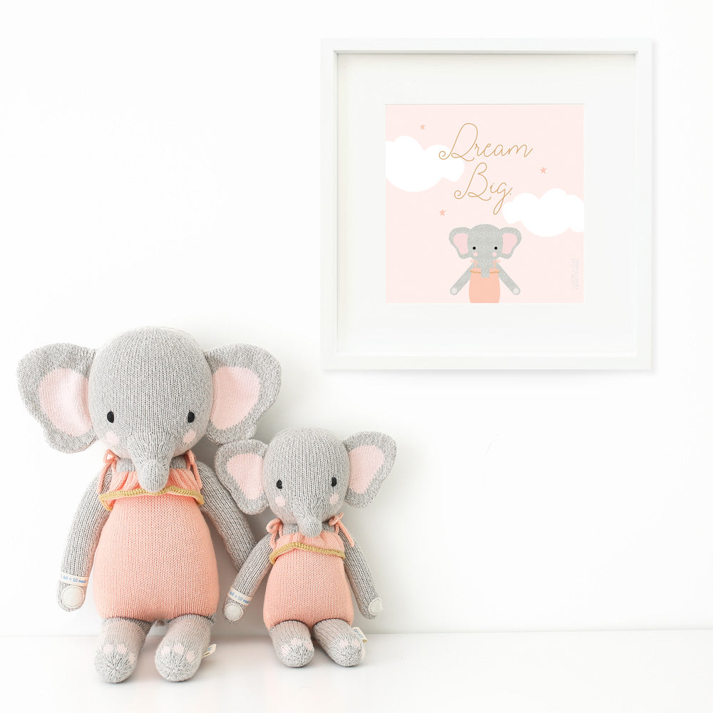 Two Eloise the elephant stuffed dolls sitting beside a framed print with a picture of Eloise that says “Dream big.”