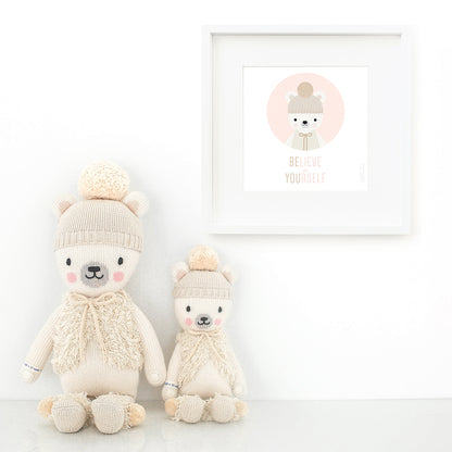 Two Stella the polar bear stuffed dolls sitting beside a framed print with a picture of Stella that says “Believe in yourself.”