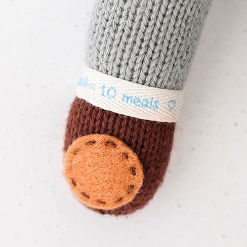 A close-up showing Oliver’s 1 doll = 10 meals wristband and the hand-knit details on his paw.