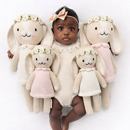A baby with her arms around four Hannah the bunny dolls in ivory and blush, in the little and regular sizes.