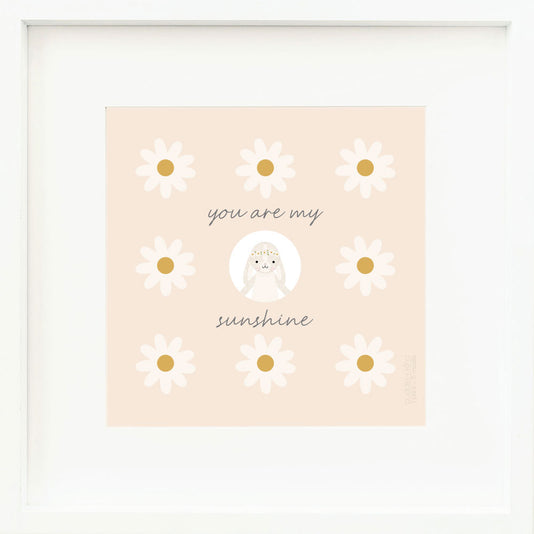 An inspirational print with a graphic of Hannah the bunny in ivory, on a light orange background decorated with daisies and the words “You are my sunshine” in dark gray.
