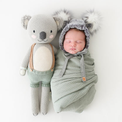 A sleeping baby wearing a koala hood with a Quinn the koala doll.