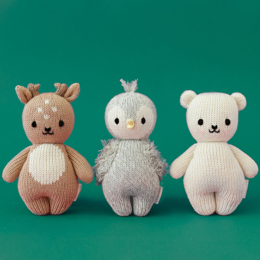 Three baby animal stuffed dolls standing in a row: baby fawn, baby penguin and baby polar bear.