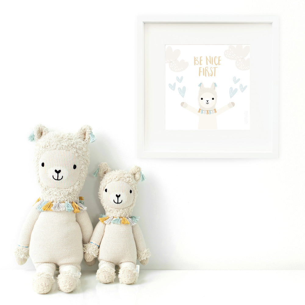 Two Lucas the llama stuffed dolls sitting beside a framed print with a picture of Lucas that says “Be nice first.”